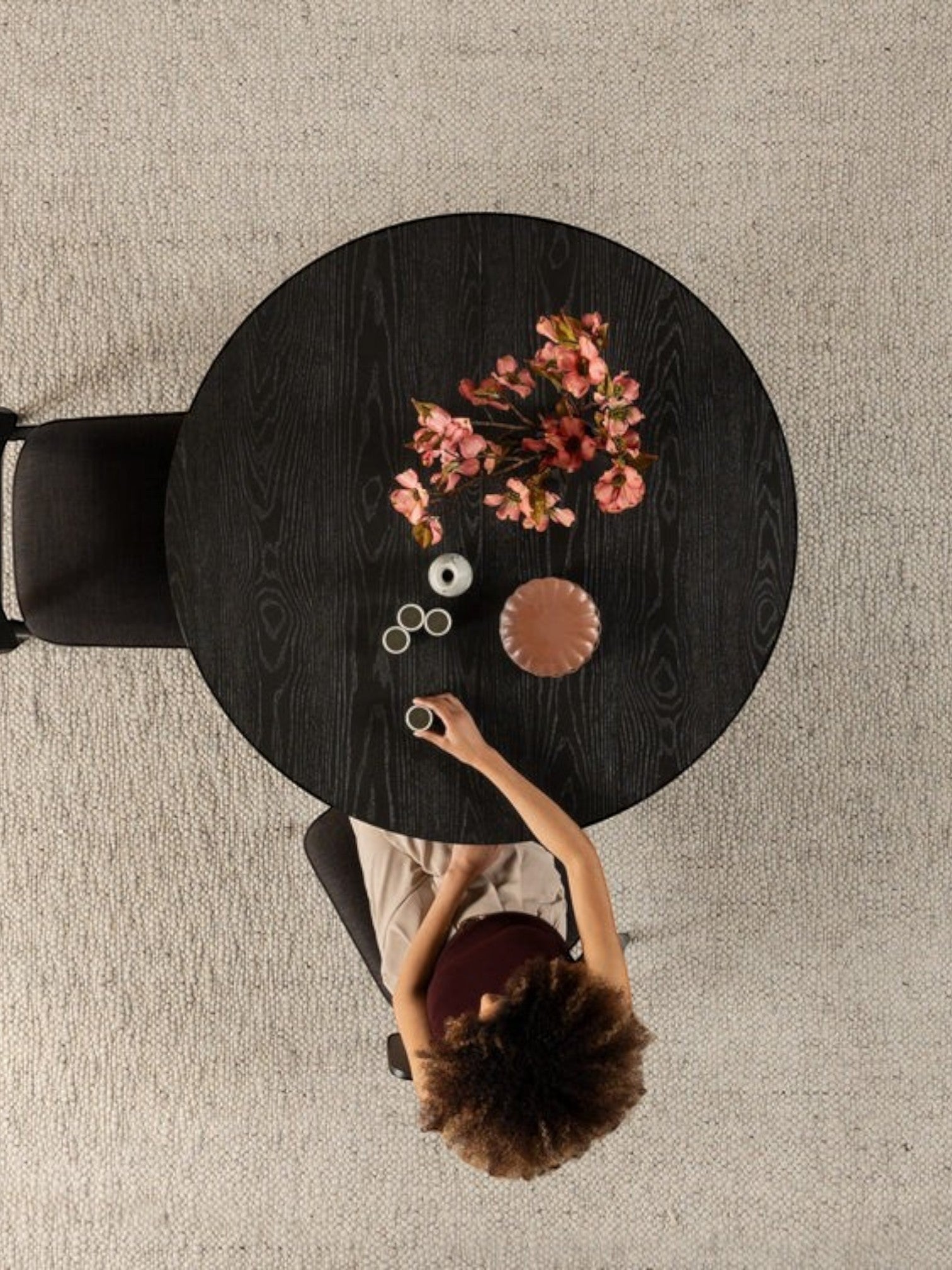 Table ronde en bois noir fumé TOCO Meubles avec fleurs roses et une femme buvant du café.