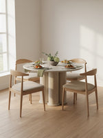 Table de salle à manger ronde TOCO Meubles Sofia avec plateau effet travertin et pied sculptural dans une pièce claire
