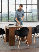 Table de salle à manger Transformer Table en noyer américain par TOCO Meubles, avec 4 chaises noires et un homme préparant la table.
