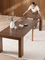 Table de salle à manger extensible en bois de noyer américain par TOCO Meubles, avec une femme ajustant une rallonge.