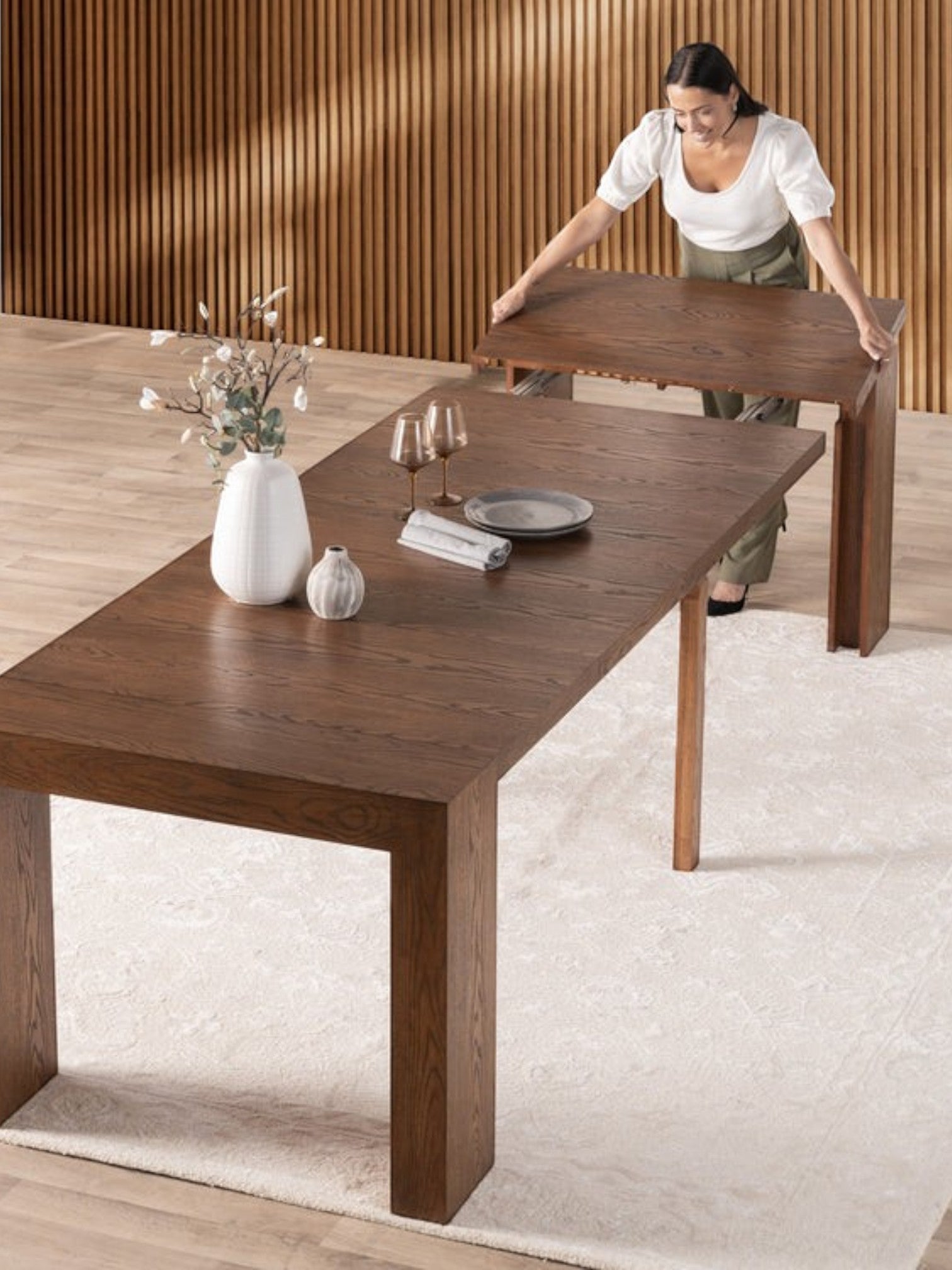 Table de salle à manger extensible en bois de noyer américain par TOCO Meubles, avec une femme ajustant une rallonge.