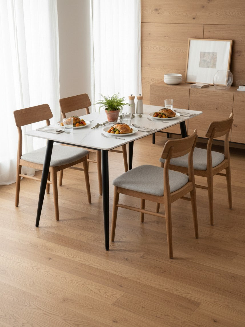 Table de salle à manger Adria par TOCO Meubles avec plateau blanc effet marbre et pieds noirs, entourée de chaises en bois