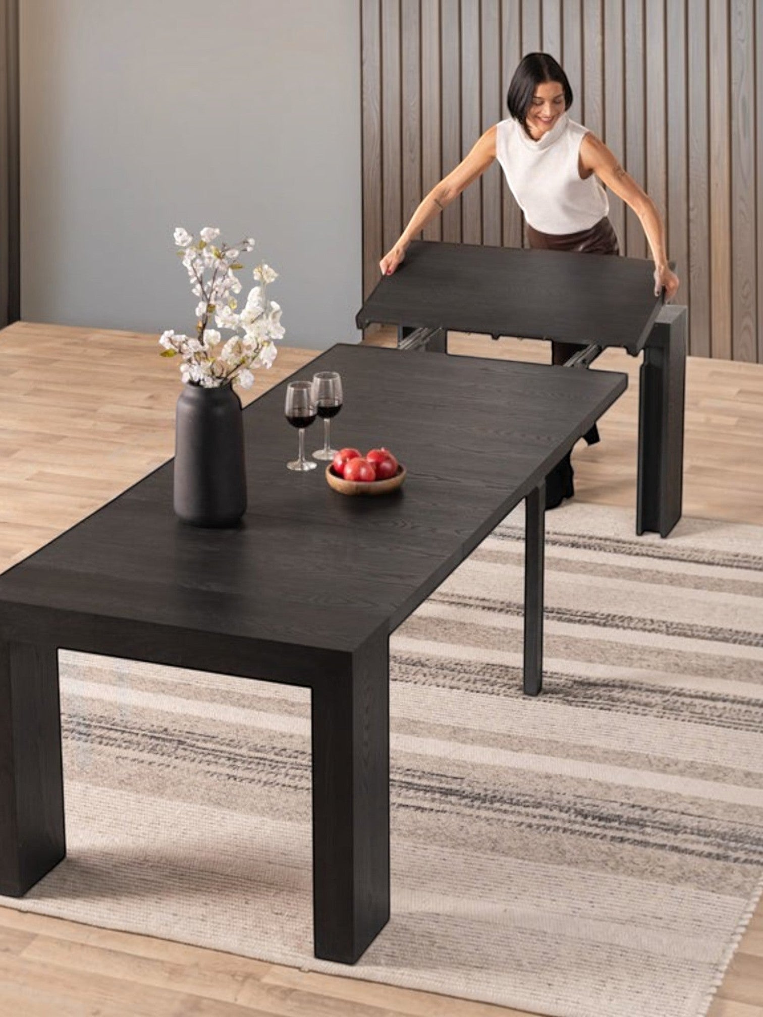 Femme installant une rallonge sur la table de salle à manger extensible TOCO Meubles en bois hickory fumé noir