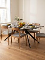 Table de salle à manger extensible Julia de TOCO Meubles avec plateau noir et pieds en métal, entourée de chaises en bois