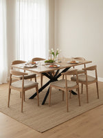 Table de salle à manger Olina par TOCO Meubles avec plateau en bois clair et pieds en métal noir, entourée de chaises