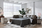 TOCO Meubles Sofa-lit Zuri marron en cuir, convertible en lit, avec couette grise et coussins décoratifs.