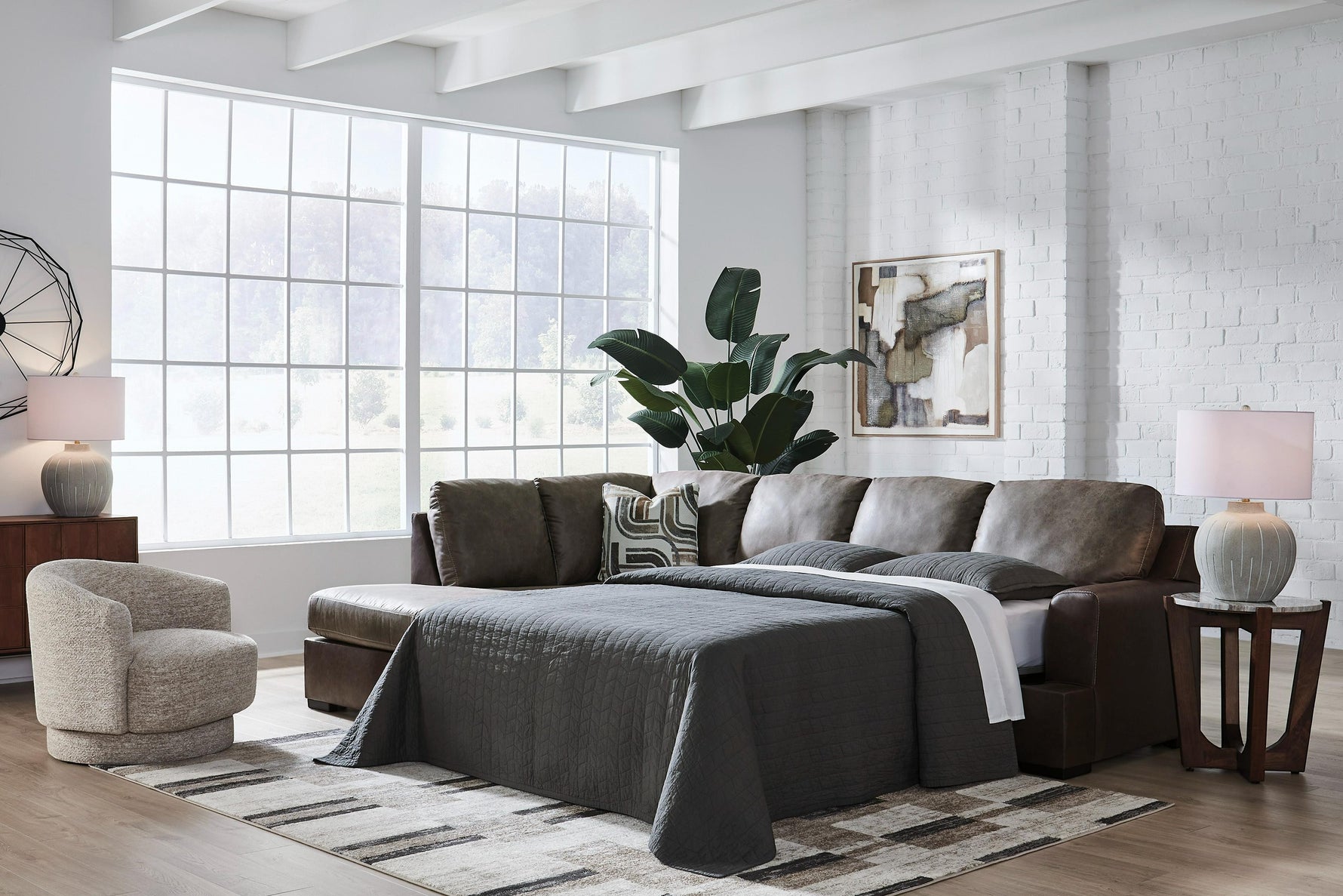 TOCO Meubles Sofa-lit Zuri marron en cuir, convertible en lit, avec couette grise et coussins décoratifs.